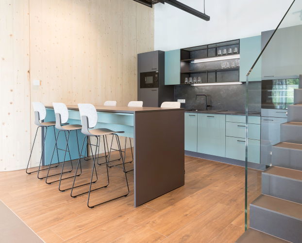 Moderne Teeküche mit Bartisch, fünf Barhockern und Treppe mit Glasgeländer.