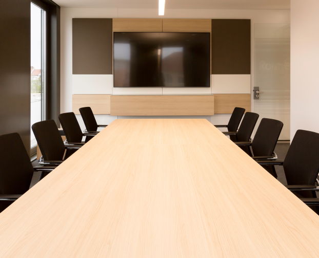 Konferenzraum mit langem Besprechungstisch, schwarzen Stühlen und integriertem Bildschirm