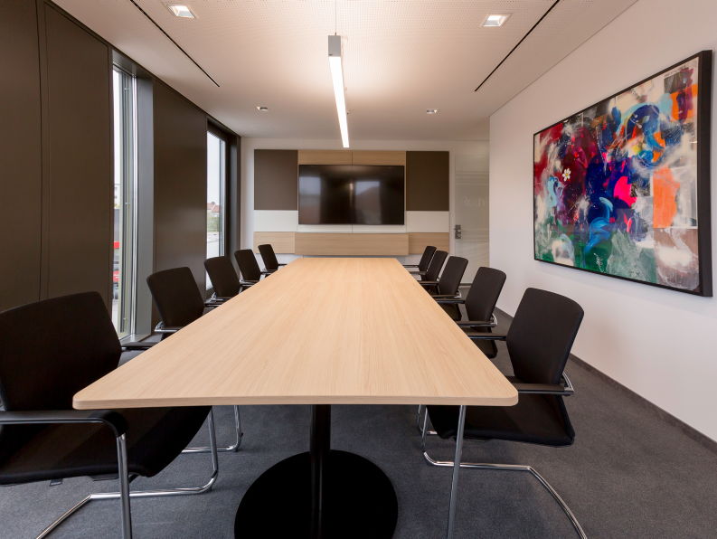 Besprechungsraum mit langem Konferenztisch, schwarzen Freischwinger Stühlen und farbenfrohem Wandbild