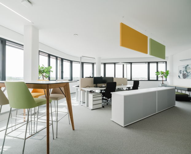 Open Office mit Stehtisch, farbigen Hockern und Blick auf moderne Arbeitsplätze.