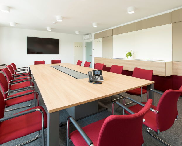 Großer Konferenztisch mit roten Freischwingern und Wandpaneelen
