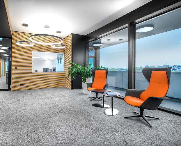 Zwei orangefarbene Hochlehnsessel in einer Loungeecke mit Rundtisch und Glasfassade