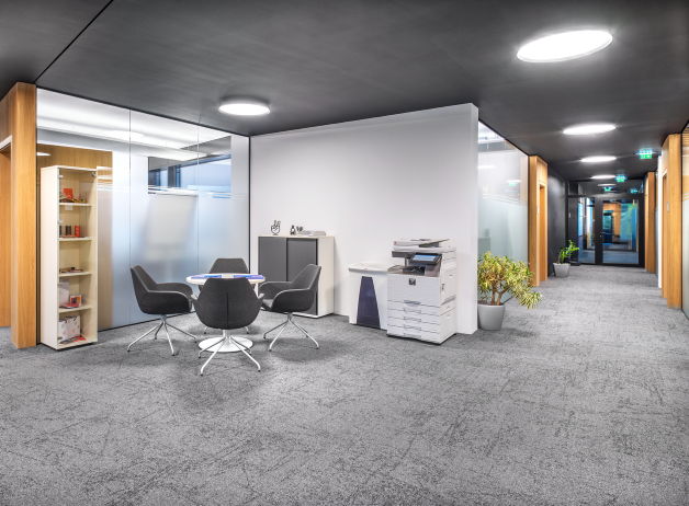 Lounge-Bereich mit vier schwarzen Sesseln, rundem Besprechungstisch und angrenzender Druckerstation im Büroflur