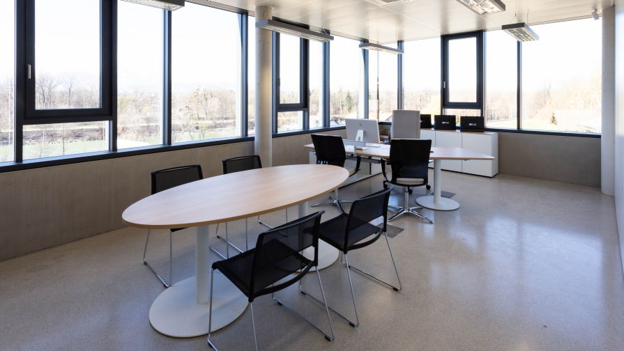 Helles Büro mit ovalem Konferenztisch, sechs schwarzen Besucherstühlen und großzügiger Fensterfront