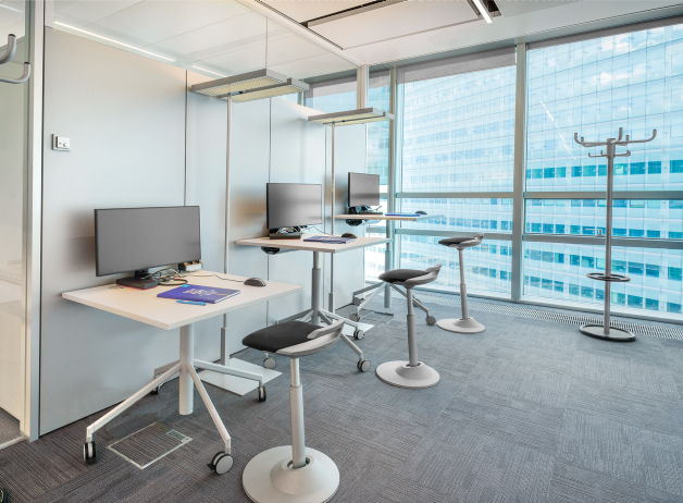 Drei moderne Arbeitsplätze mit höhenverstellbaren Tischen und ergonomischen Hockern bei STRABAG in Wien