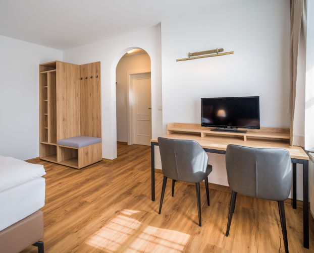 Kombination aus Schreibtisch, Fernseher und Garderobe in einem hellen Hotelzimmer mit Holzoptik
