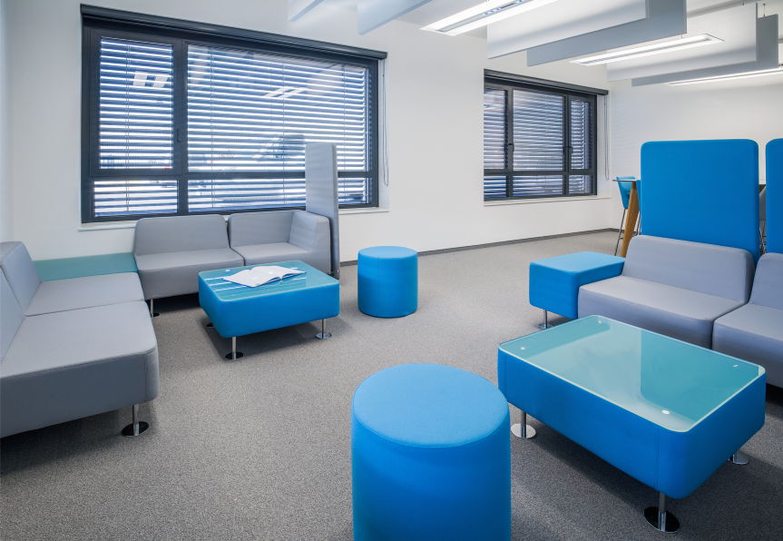 Moderne Lounge mit hellgrauen Sofas, blauen Hockern und Couchtischen in der STRABAG AG St. Pölten