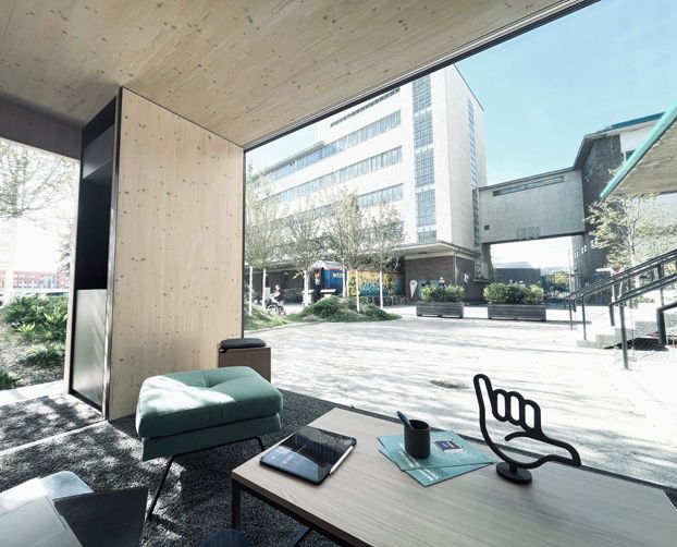 Innenansicht eines Meeting Cubes mit Tisch, Hocker und Panoramablick auf den urbanen Außenbereich