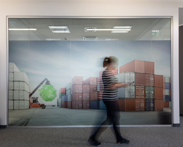 Große Fotowand mit Containerlandschaft und Person im Gang eines modernen Bürogebäudes