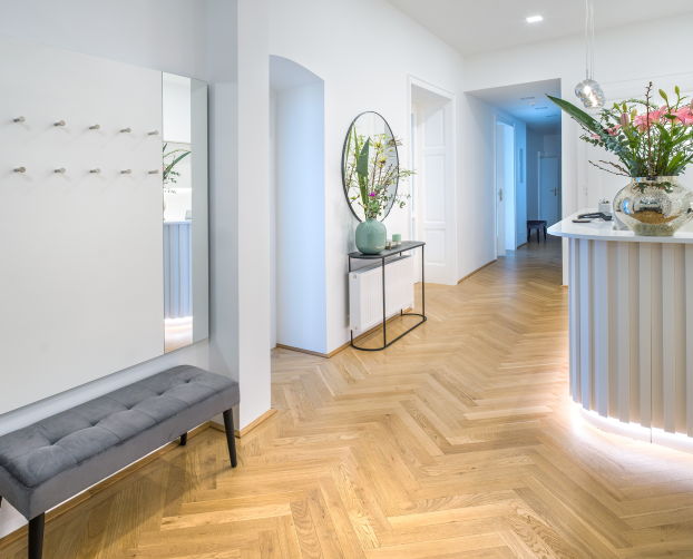 Heller Flur mit grauer Sitzbank, Spiegel, filigranem Sideboard und dekorativen Blumen in Vase