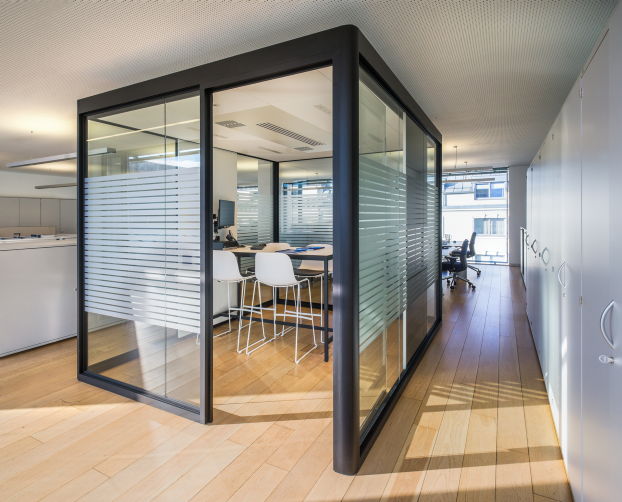 Hochtisch mit vier weißen Barhockern und Monitor in abgeschlossener Meetingbox