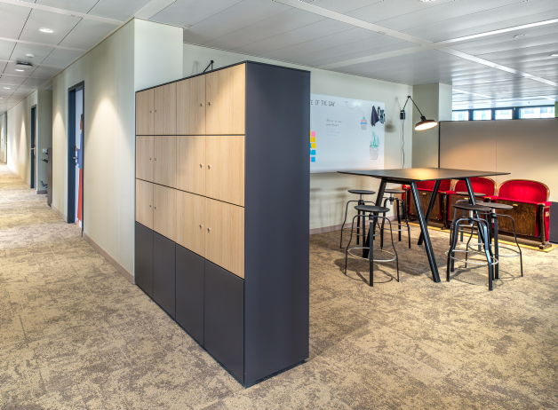 Informelle Besprechungszone mit Stehtisch, Barhockern und Stauraumwand in modernem Design.