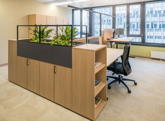 Heller Büroarbeitsplatz mit integrierter Stauraumeinheit und grünem Pflanzenmodul als visuelle und funktionale Raumtrennung.
