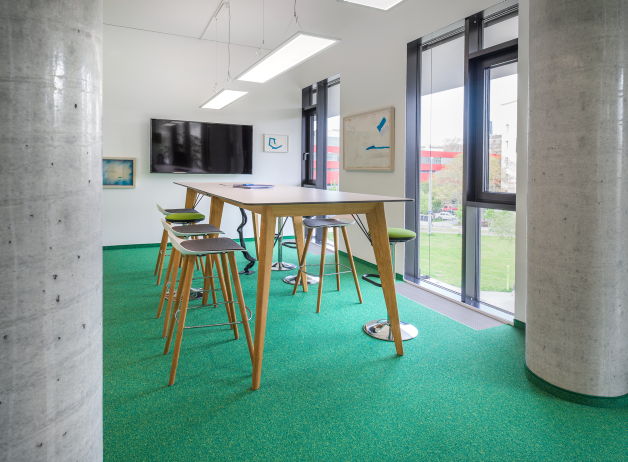 Heller Meetingraum mit grünem Teppichboden, Hochtisch und Designer-Barhockern bei Risk Experts
