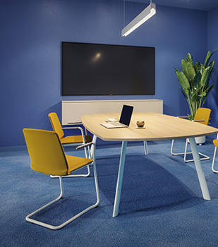 Besprechungsraum mit gelben Curve Stühlen und großem Bildschirm an blauer Wand.