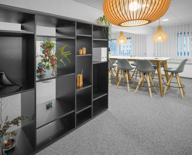 Schwarzes Regal als Raumtrenner, dahinter Hochtisch mit Barhockern und Designerlampen