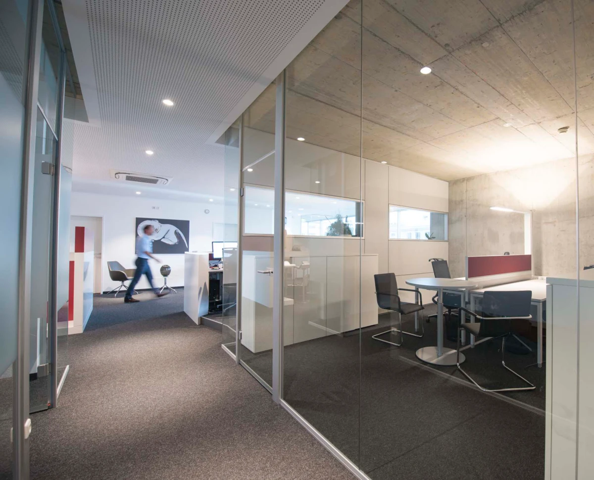 Offener Büroflur mit Glaswänden, Einblick in Arbeitsplatzbereich mit Schreibtisch und Stauraum