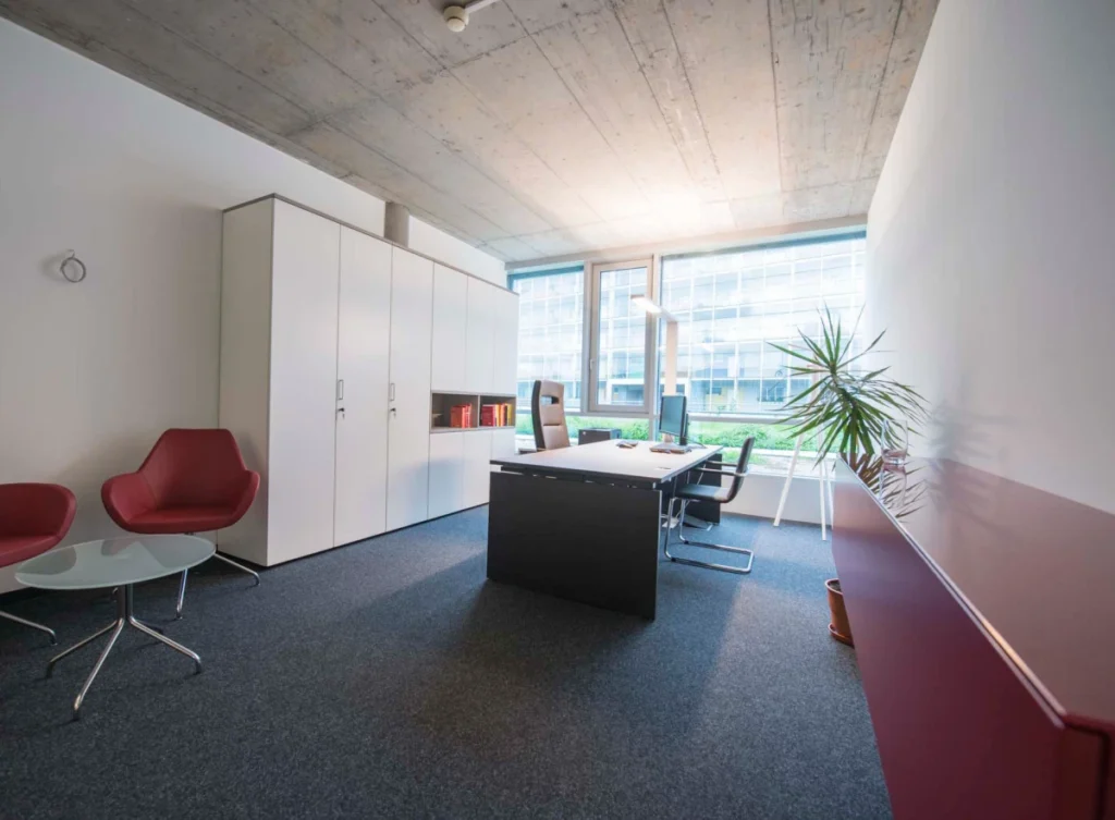 Lichtdurchflutetes Einzelbüro mit schwarzem Tisch, weißen Schränken und roten Lounge-Sesseln