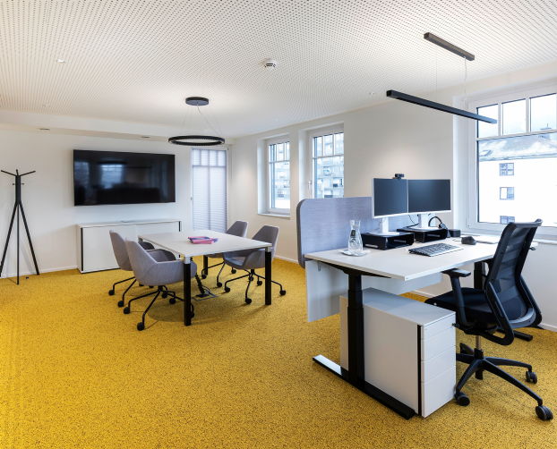 Arbeitsplatz mit Sitz-Steh-Tisch und angrenzender Besprechungszone.