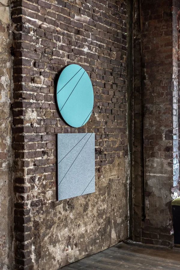 Runde und eckige AOS CrazyPanel Wandabsorber in Grau und Türkis an einer Backsteinwand