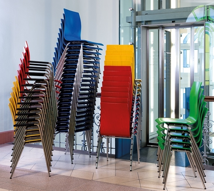 Ambientebild von stapelbaren Stühlen Mega von Kilpper mit 4-Fuß Gestellen aus Metall und Sitzschalen aus Holz in bunten Farben. Einfach stapelbar, vielseitig anwendbar.