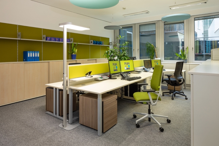 Open Space Office mit Sichtschutz mit Pinnwand in grün und Rollcontainer in Holzoptik.