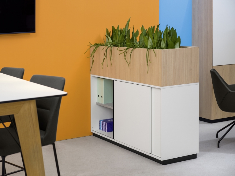 Ambiente Produktbild Schiebetürenschrank in Melamin Farbe weiß mit Blumenwannen-Aufsatz Evergreen für Bürobegrünung in Eichenoptik.