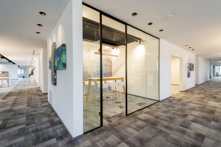 Glastrennwand zur Schaffung eines Meetingraumes zwischen zwei weißen Wänden.