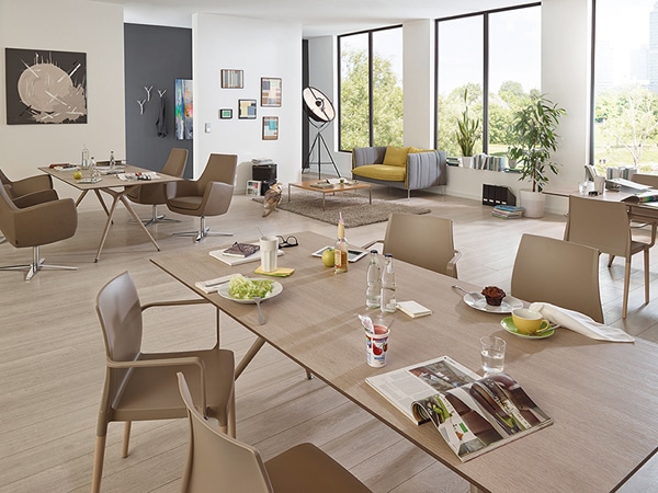Ambientebild Aufenthaltsbereich ausgestattet mit Stühlen Blunt von Pedrali mit 4-fuß Gestell aus Holz und Sitzschale aus Kunststoff mit Armlehnen in beige.
