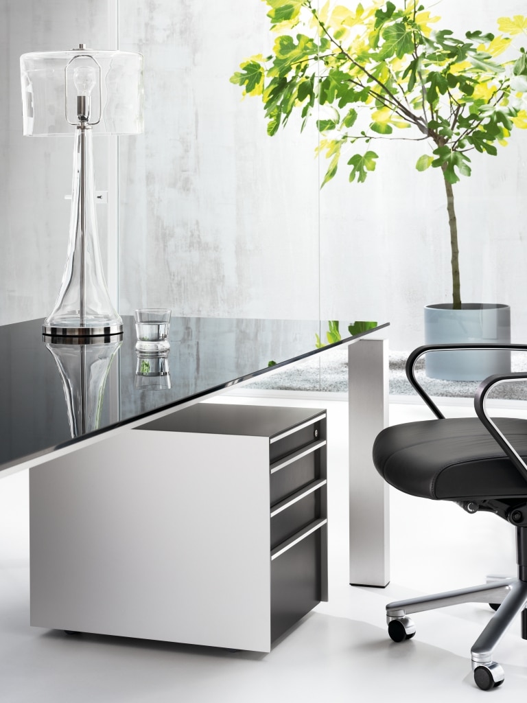 Arbeitstisch der Produktserie s800 für Chefbüros mit einem Tischgestell in Silber und einer Tischplatte aus dunklem Glas.