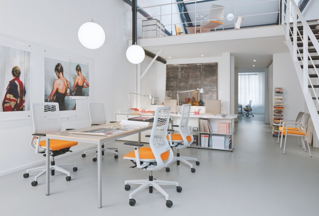 Open Space Office mit Drehstühlen Mera von Klöber mit weißem Gestell und schwarzen Rollen sowie weißem Netzrücken und orangem Sitzkissen.