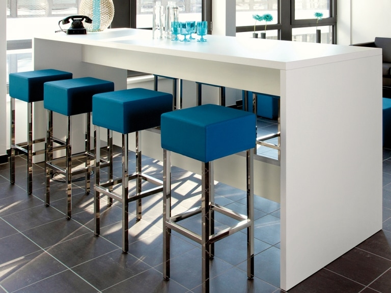 Ambientebild Meetingbereich mit Stehtisch und Barhockern KirRoyal der Marke SMV mit glänzendem Metallgestell und gepolsterten Sitzflächen in royalblauer Lederoptik.