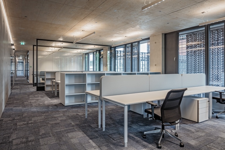 Großraumbüro mit 6er Arbeitsplätzen und Raumteilung in Form von Regalen in Weiß- und Grautönen.
